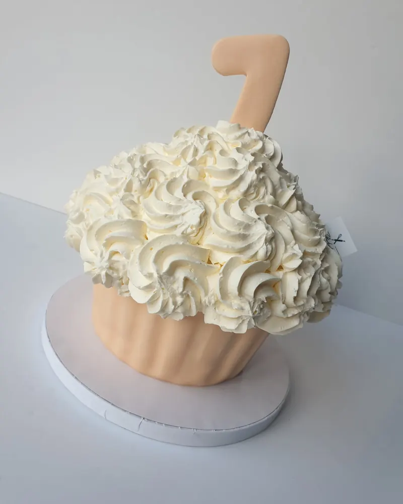 Perzikkleurige reuzecupcake-taart met vanillerozetten en cijfer 1